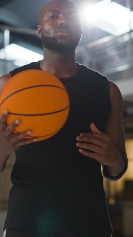 Vertikale-Videoporträtaufnahme-Eines-Männlichen-Basketballspielers-Auf-Dem-Spielfeld,-Der-Den-Ball-Mit-Blendenfleck-Unter-Dem-Arm-Hält